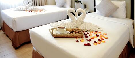 Two neatly made beds with white linens, a tray with a cup and pastries, and rose petals scattered on the bed.