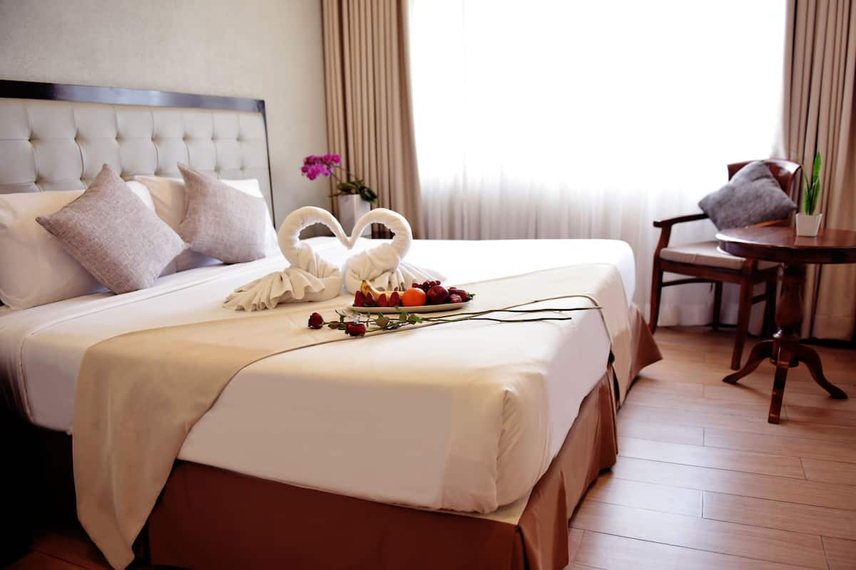 A hotel room with a neatly made bed, a dining table with a chair, and a vase with flowers.