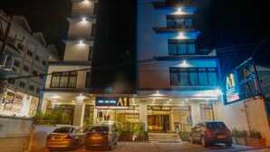 A multi-story hotel with a modern design, featuring a prominent entrance and several cars parked in front. - Aura One Hotel (Baguio)