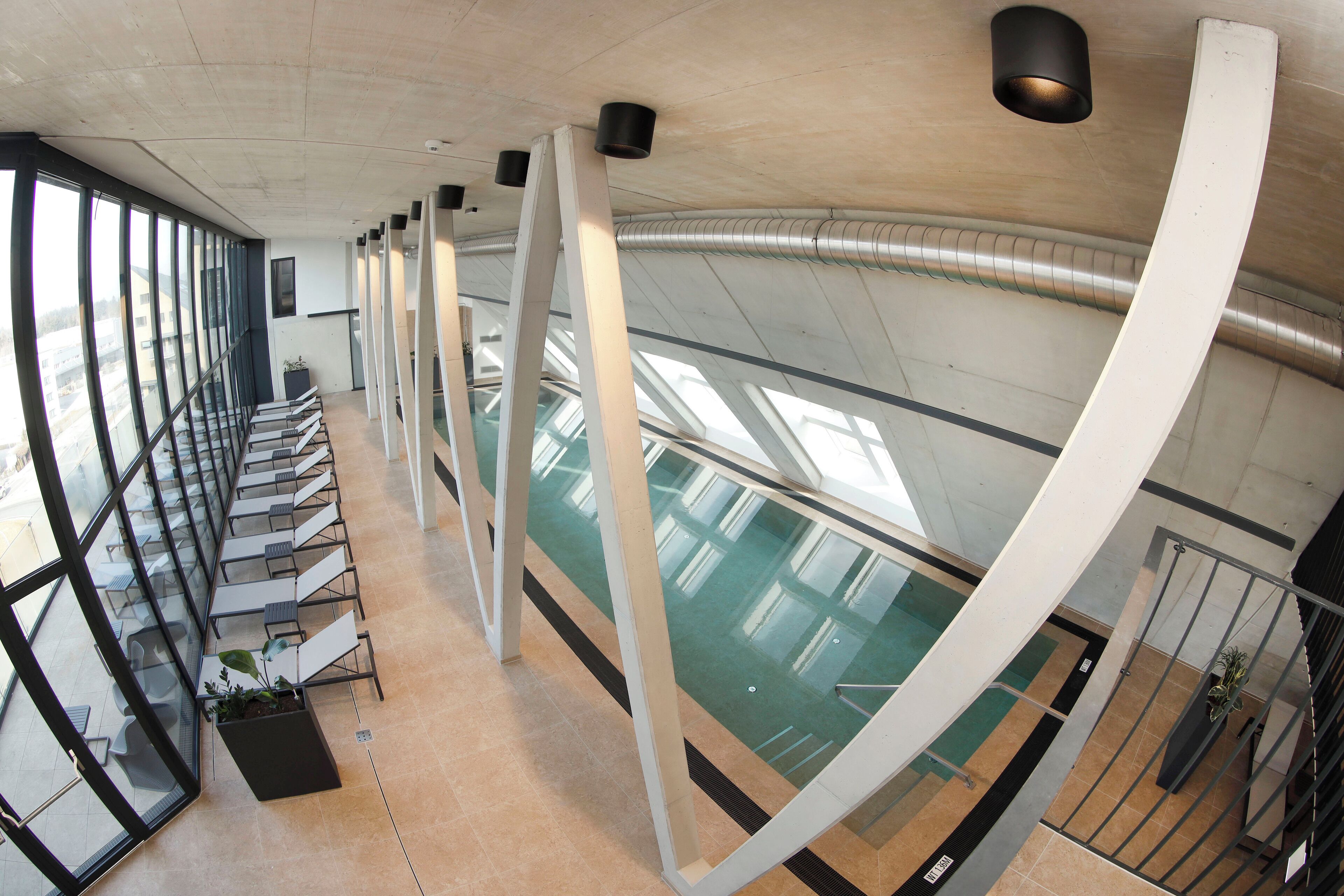 Un espace intérieur moderne doté d’un plafond incurvé, de grandes fenêtres et d’un espace piscine.