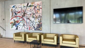 A lobby with a large abstract painting, three beige sofas, a small black table, and a large window.