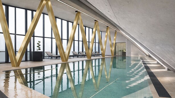 Une piscine intérieure au design moderne, dotée d’une structure dorée originale et de chaises longues.