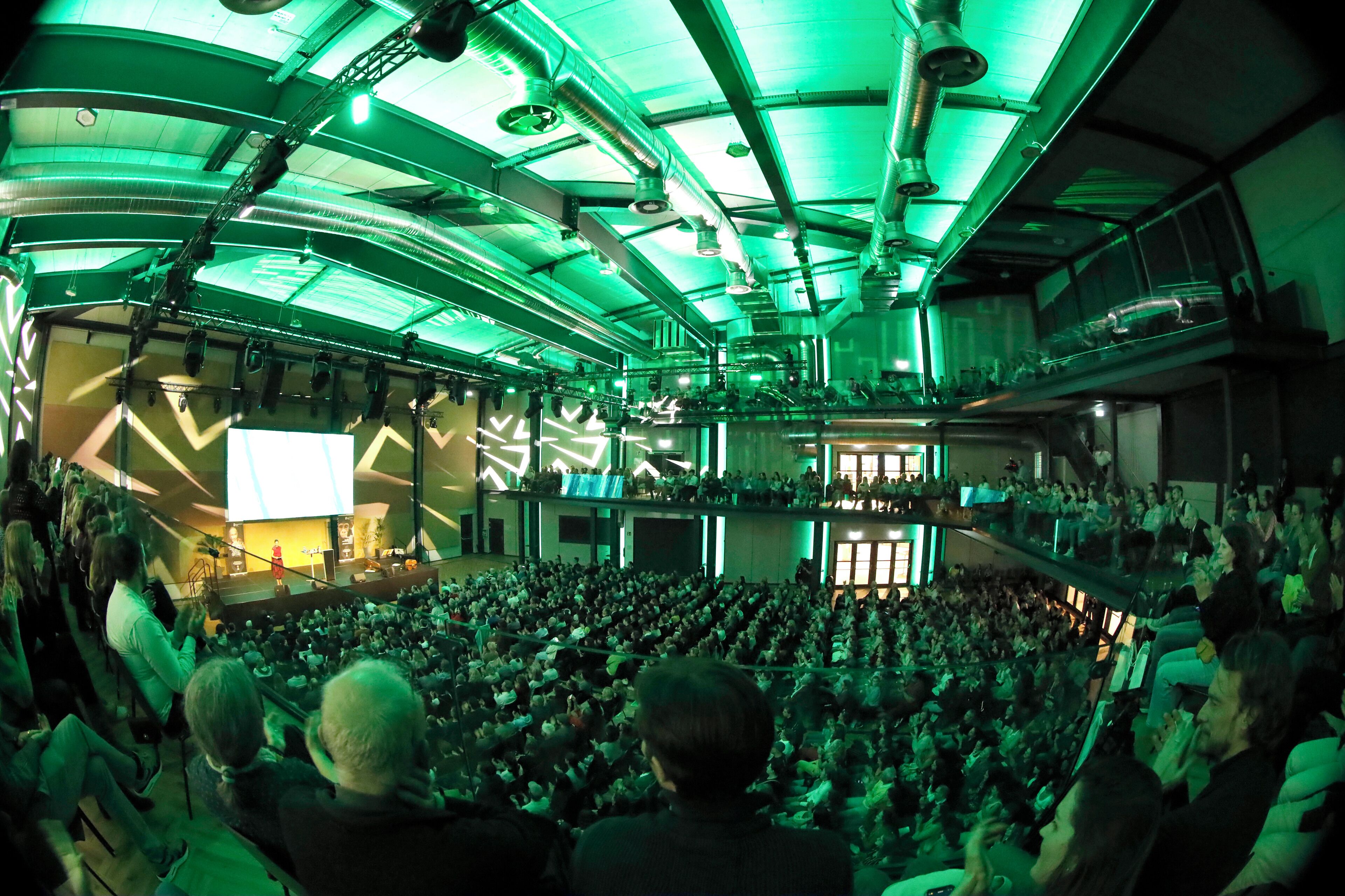A large indoor auditorium with a high ceiling and green lighting.