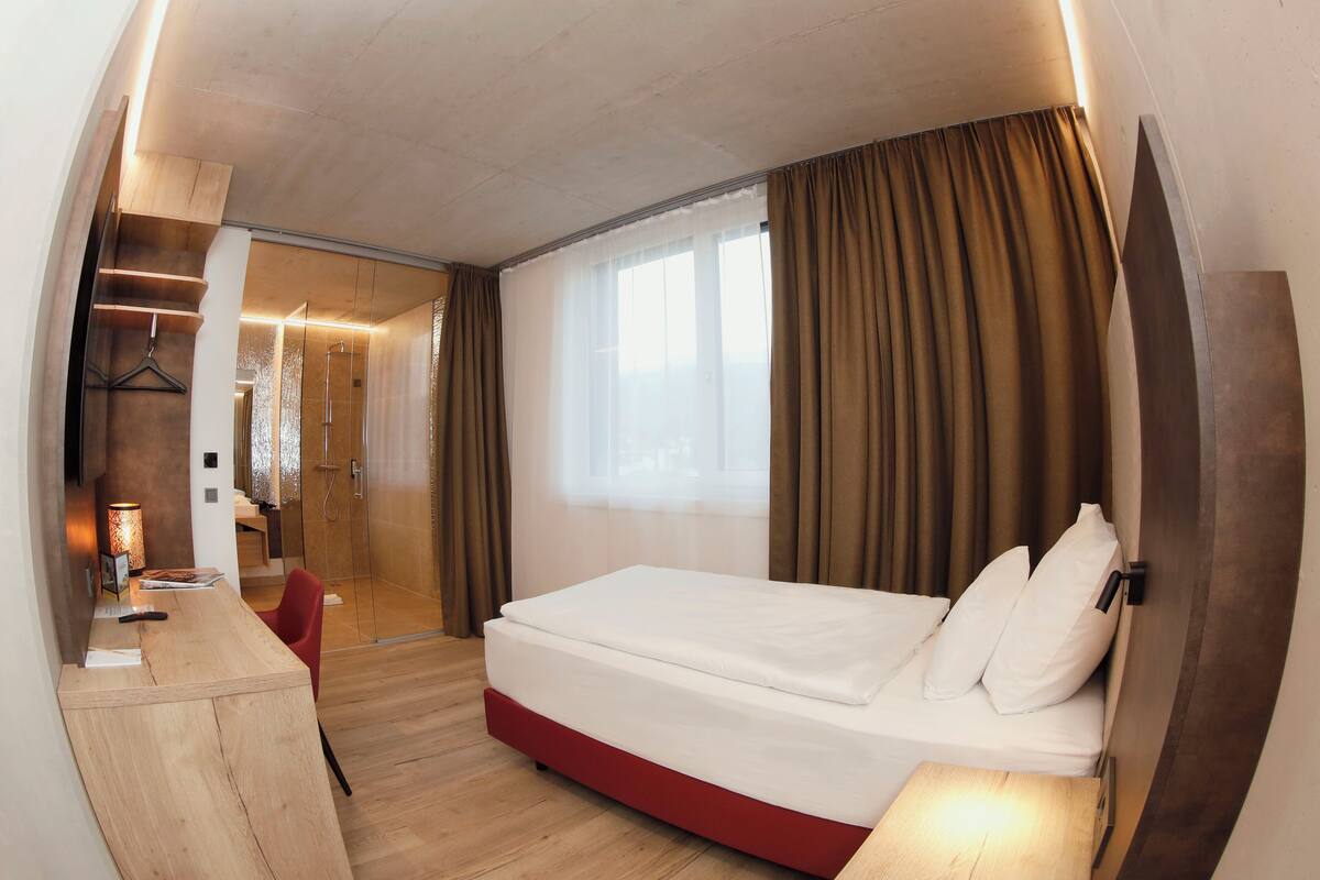 Una habitación de hotel moderna con cama, escritorio y zona de ducha.