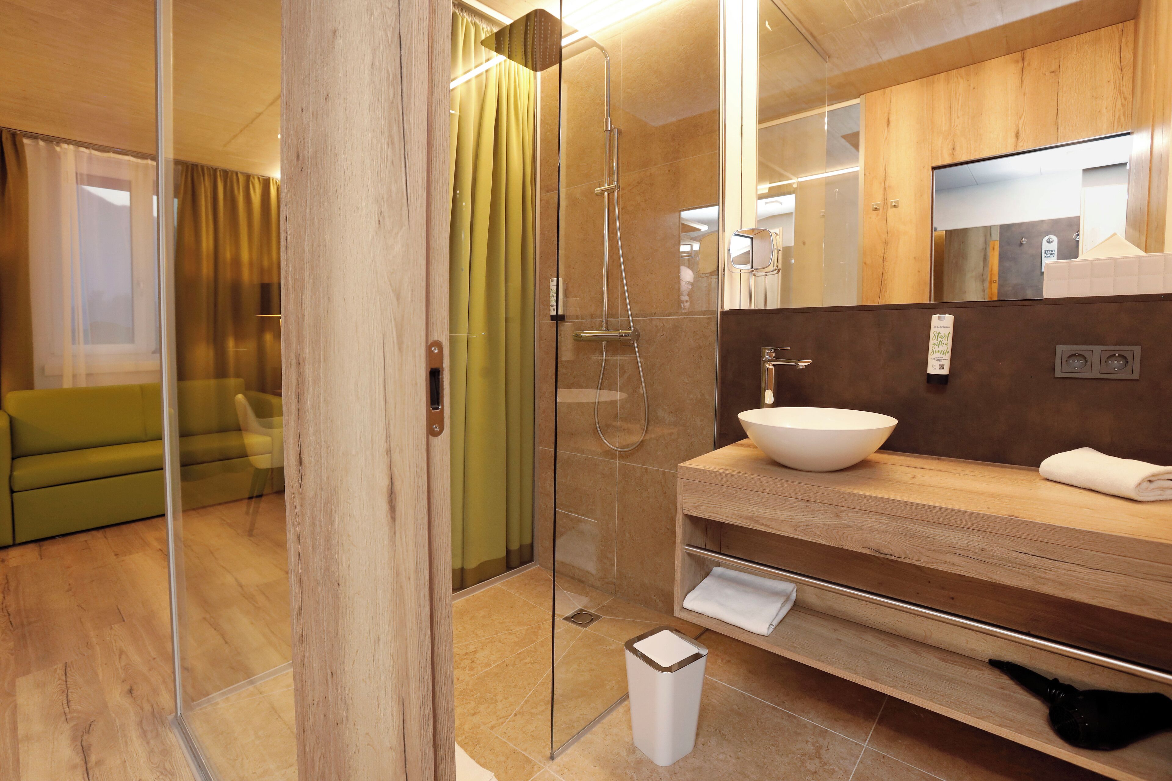 Un baño moderno con cabina de ducha de vidrio, tocador de madera con lavabo y un espejo sobre el lavabo.