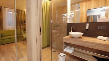 Un baño moderno con cabina de ducha de vidrio, tocador de madera con lavabo y un espejo sobre el lavabo.