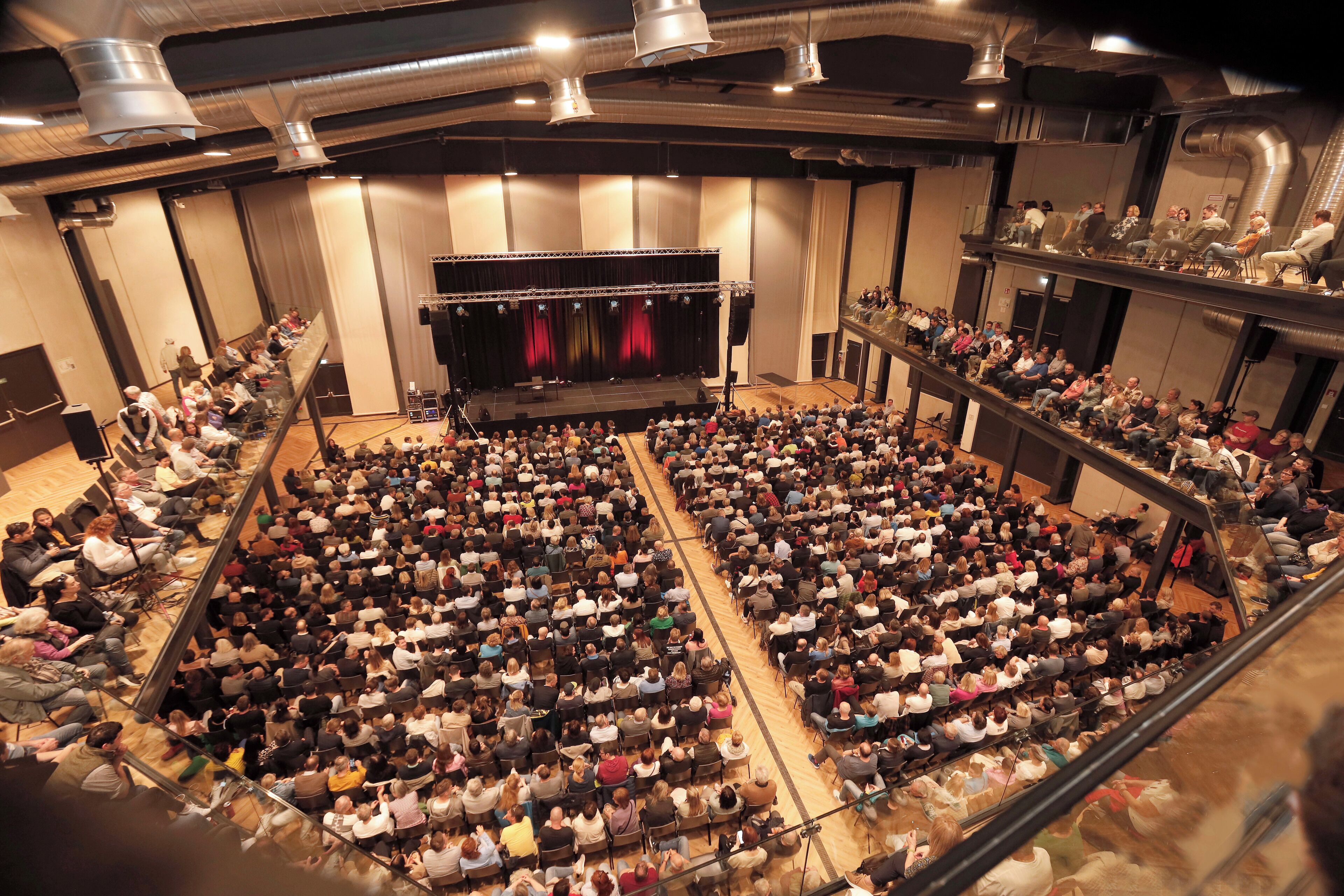 Un amplio auditorio interior con asientos escalonados, un escenario y un balcón.