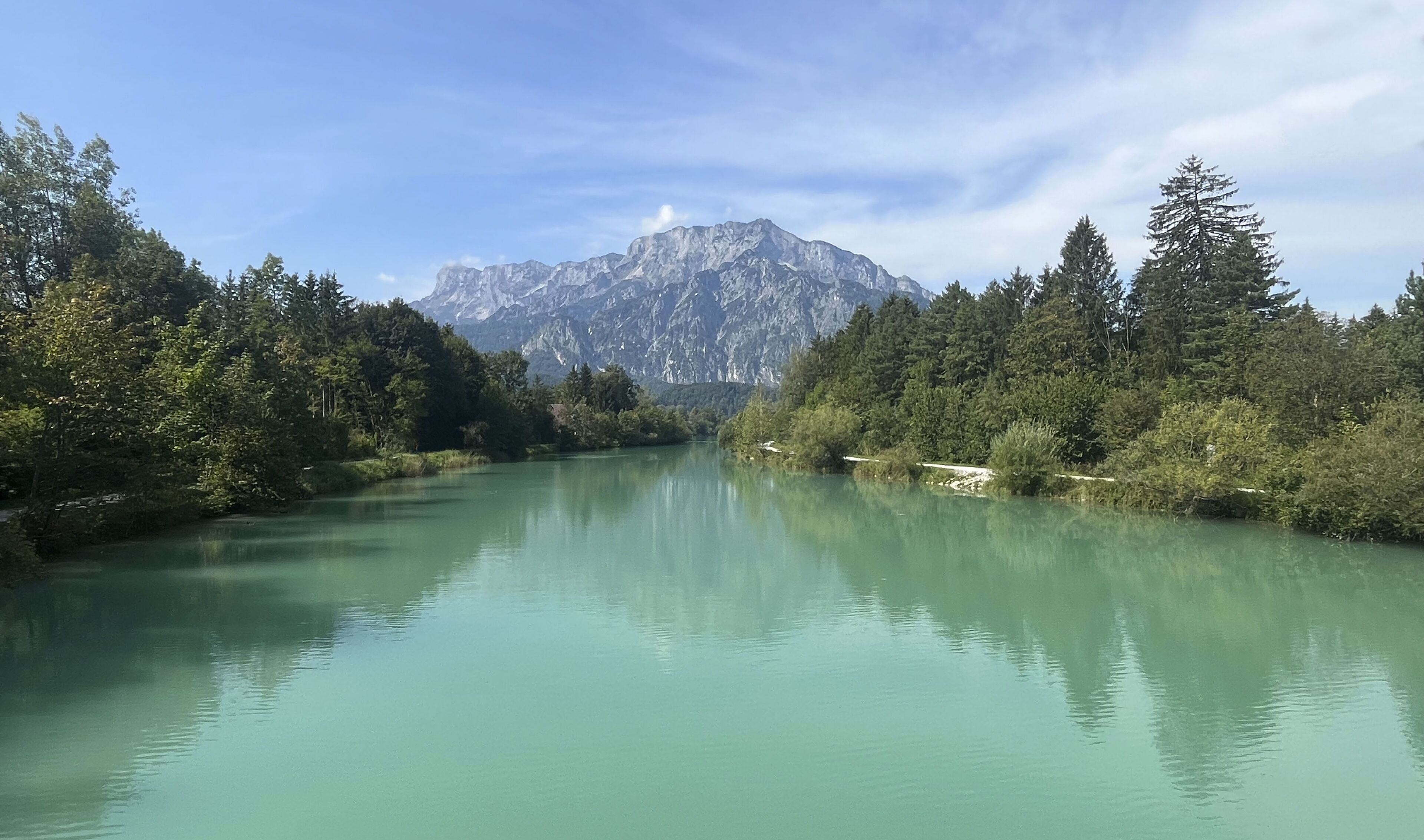 A calm river with dense forest on both sides and a mountain range in the background.