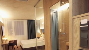 Une chambre d’hôtel comprenant un lit, un bureau, une chaise et une paroi en verre qui sépare l’espace de la douche.