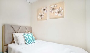 A neatly made bed with white and blue patterned pillows, a beige upholstered headboard, and two floral artwork pieces on the wall. - LUX The Elegant Palm Beach Suite (Dubai)
