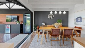 Un comedor moderno con una mesa y sillas de madera, un espejo grande y lámparas colgantes.