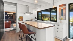Cocina moderna con una isla grande, taburetes de bar y vistas al exterior.