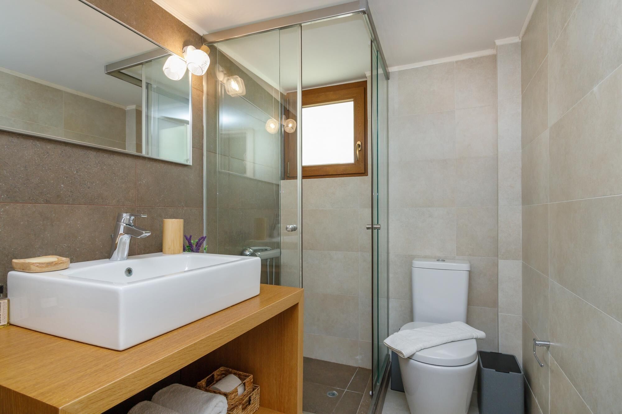A modern bathroom with a large white sink, a glass shower enclosure, and a toilet.