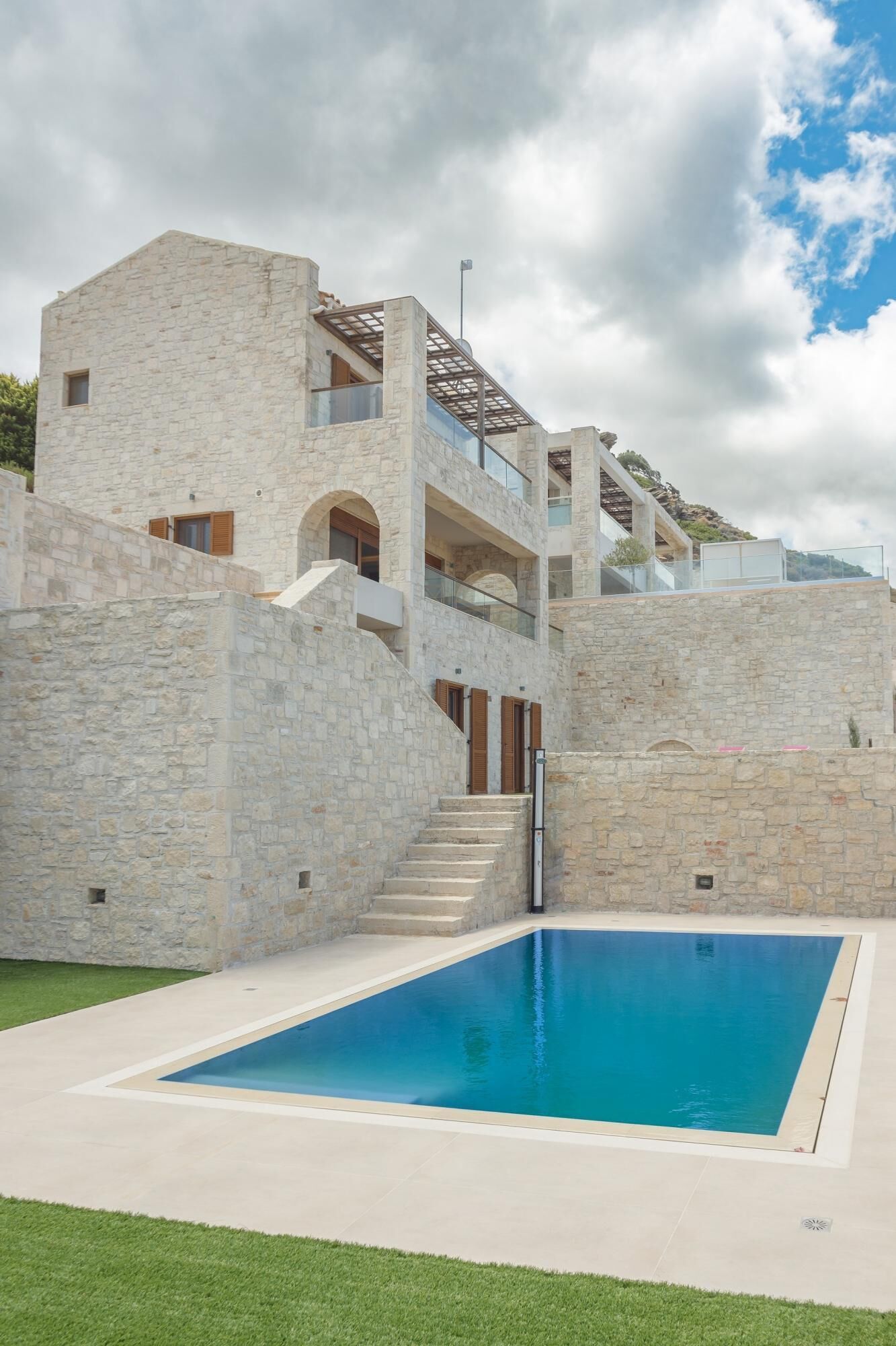 Un bâtiment moderne avec une façade en pierre, une piscine et un escalier menant à un balcon.