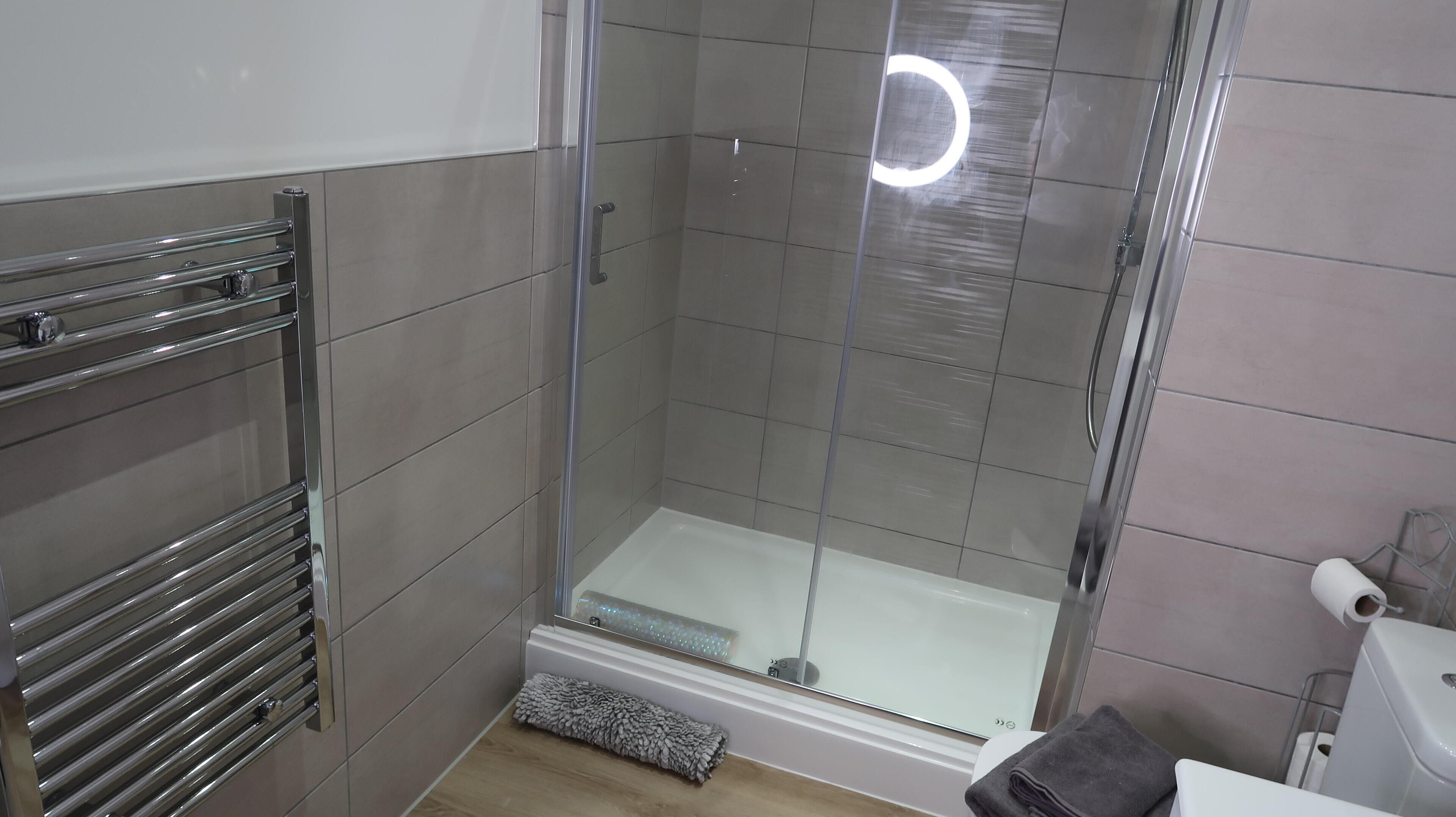 Et moderne badeværelse med en brusekabine i glas, et håndklædetørrestativ og et toilet.