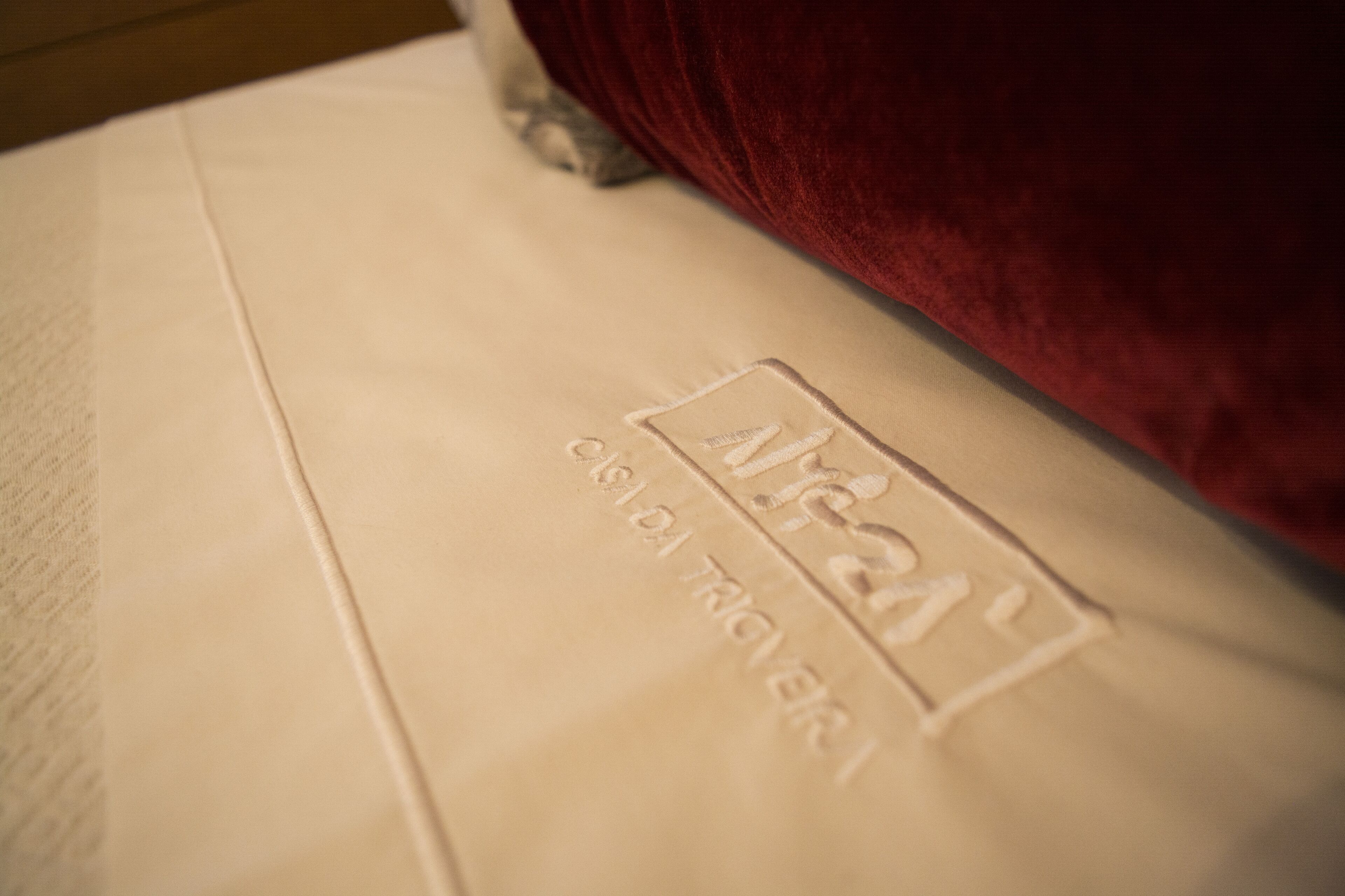 A close-up of a bed with a red headboard and a white mattress with embroidered text.