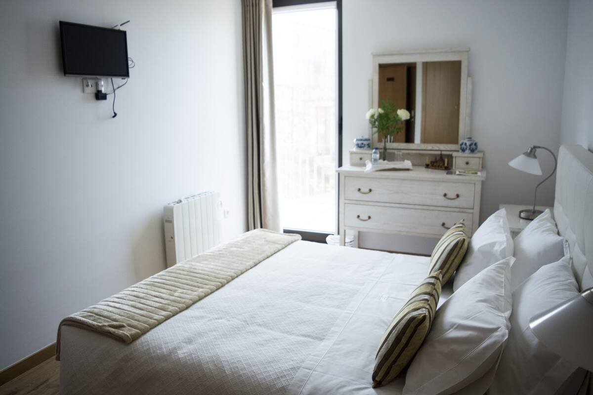 Ein Hotelzimmer mit einem Bett, einem Schminktisch, einem Spiegel und einem an der Wand montierten Fernseher.
