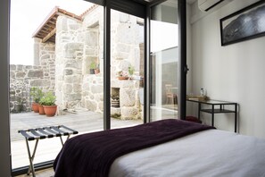 A bedroom with a bed, a window, and a view of a stone building with potted plants. - Casa da Trigueira (Alijó)