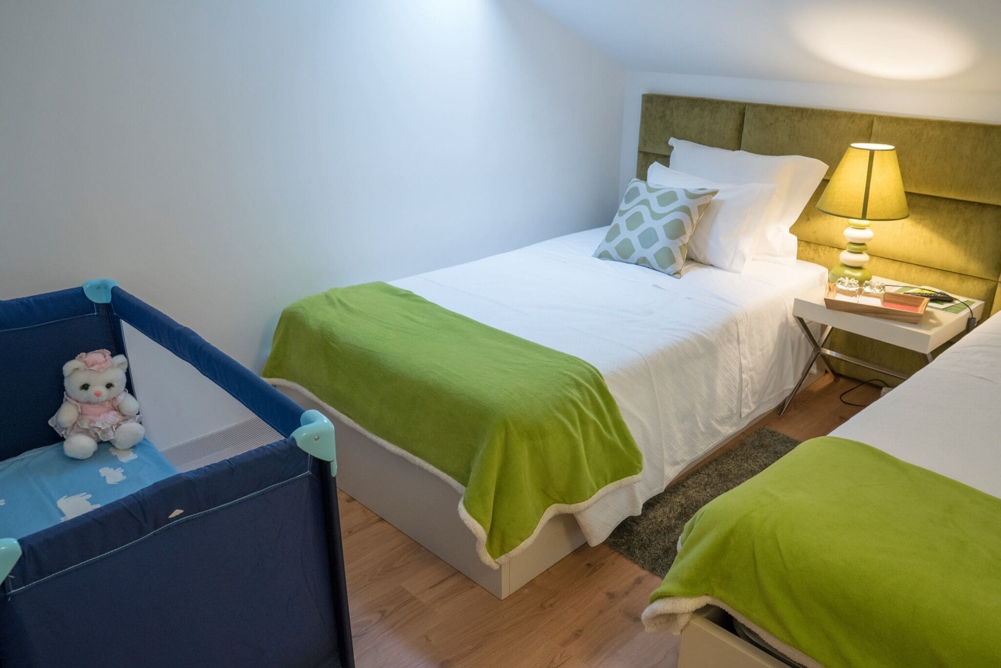 A neatly arranged bedroom with a bed, bedside table, lamp, and a small chair with a teddy bear.