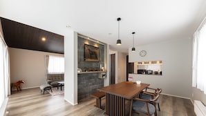 Een moderne woonkamer met een houten eettafel, een bank en een keukenhoek met een magnetron en kastjes.