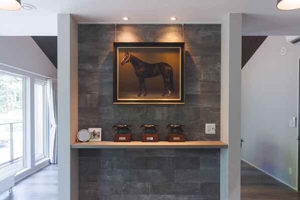 A framed horse painting on a wall, a shelf with three small boxes, and a window with curtains.