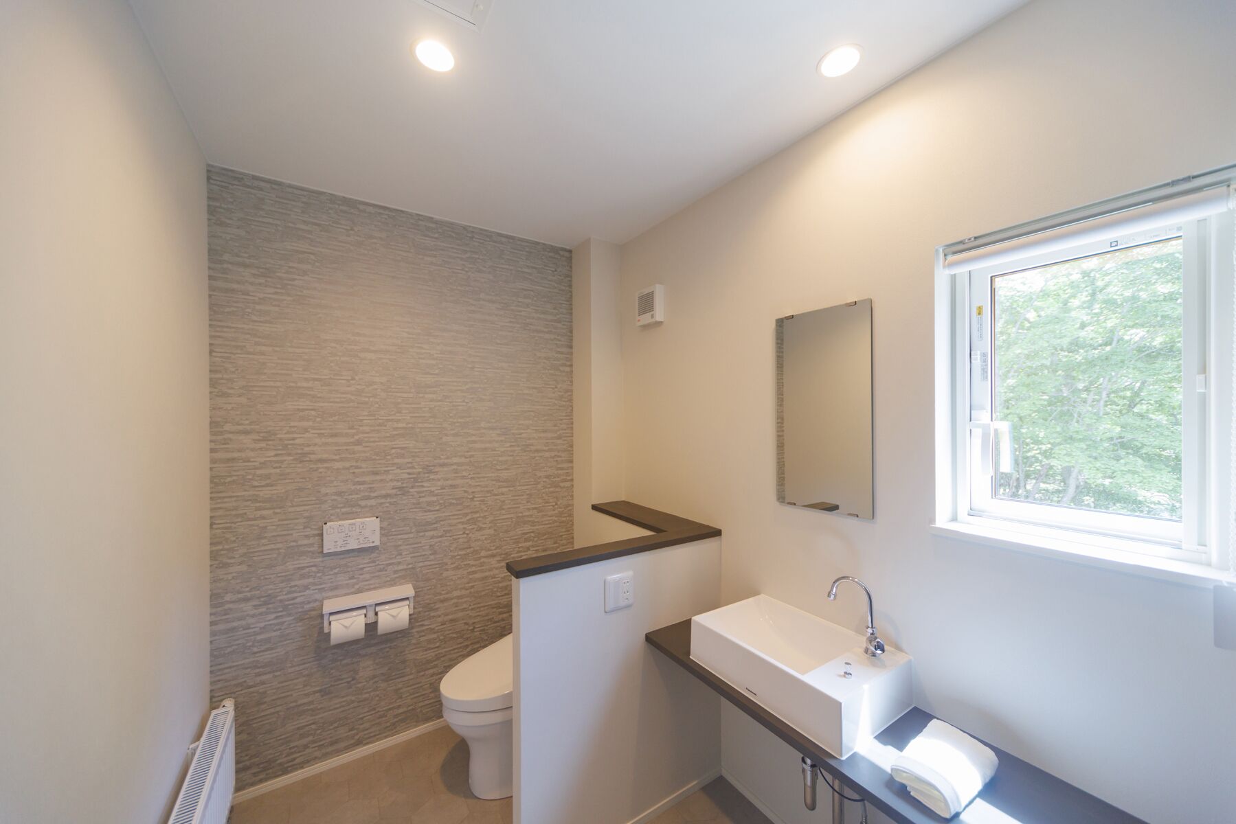 Ein modernes Badezimmer mit Toilette, Waschbecken und einem Fenster mit Tageslicht.