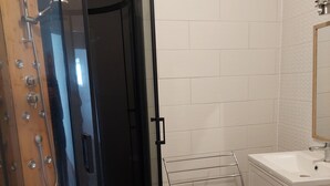 A shower enclosure with a wooden floor, a white sink, and a towel rack.