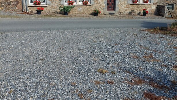 A two-story house with stone walls, multiple windows with flower boxes, and a gravel driveway.