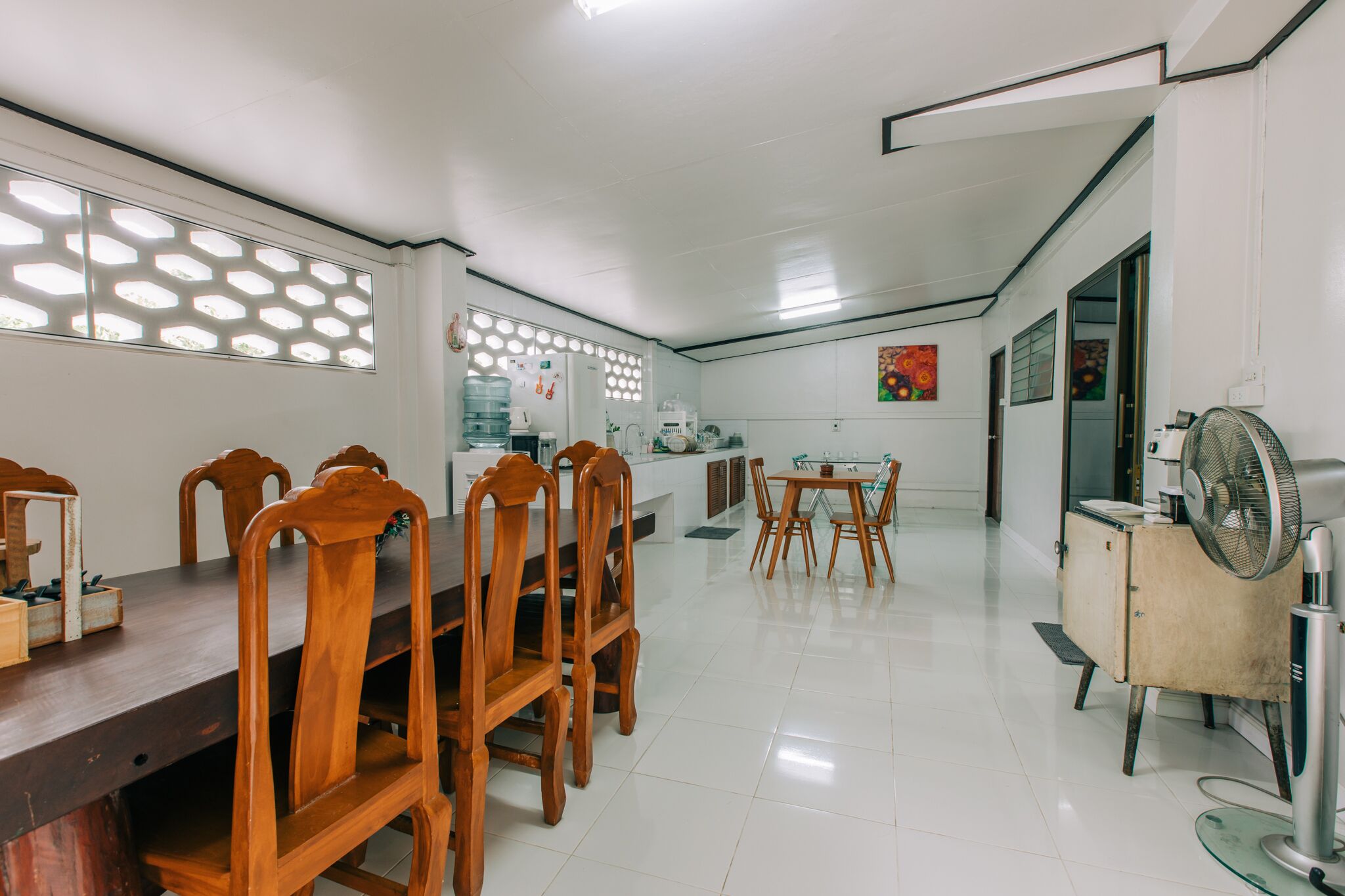 A spacious dining area with a long wooden table and chairs, a water dispenser, and a refrigerator.