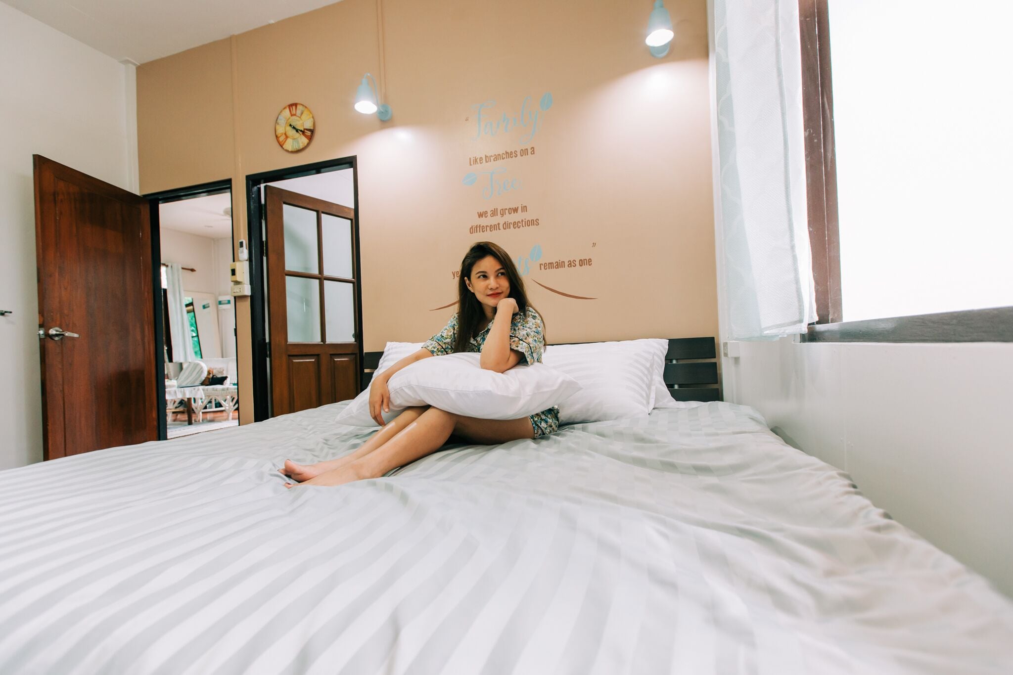 A person sitting on a bed in a room with a clock and a motivational quote on the wall.