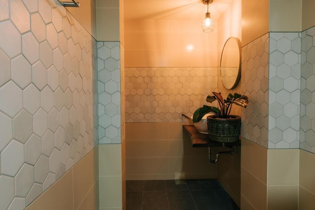 Un baño con baldosas de patrón hexagonal, un lámpara colgante, un espejo y una planta en maceta.