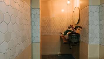 Un baño con baldosas de patrón hexagonal, un lámpara colgante, un espejo y una planta en maceta.