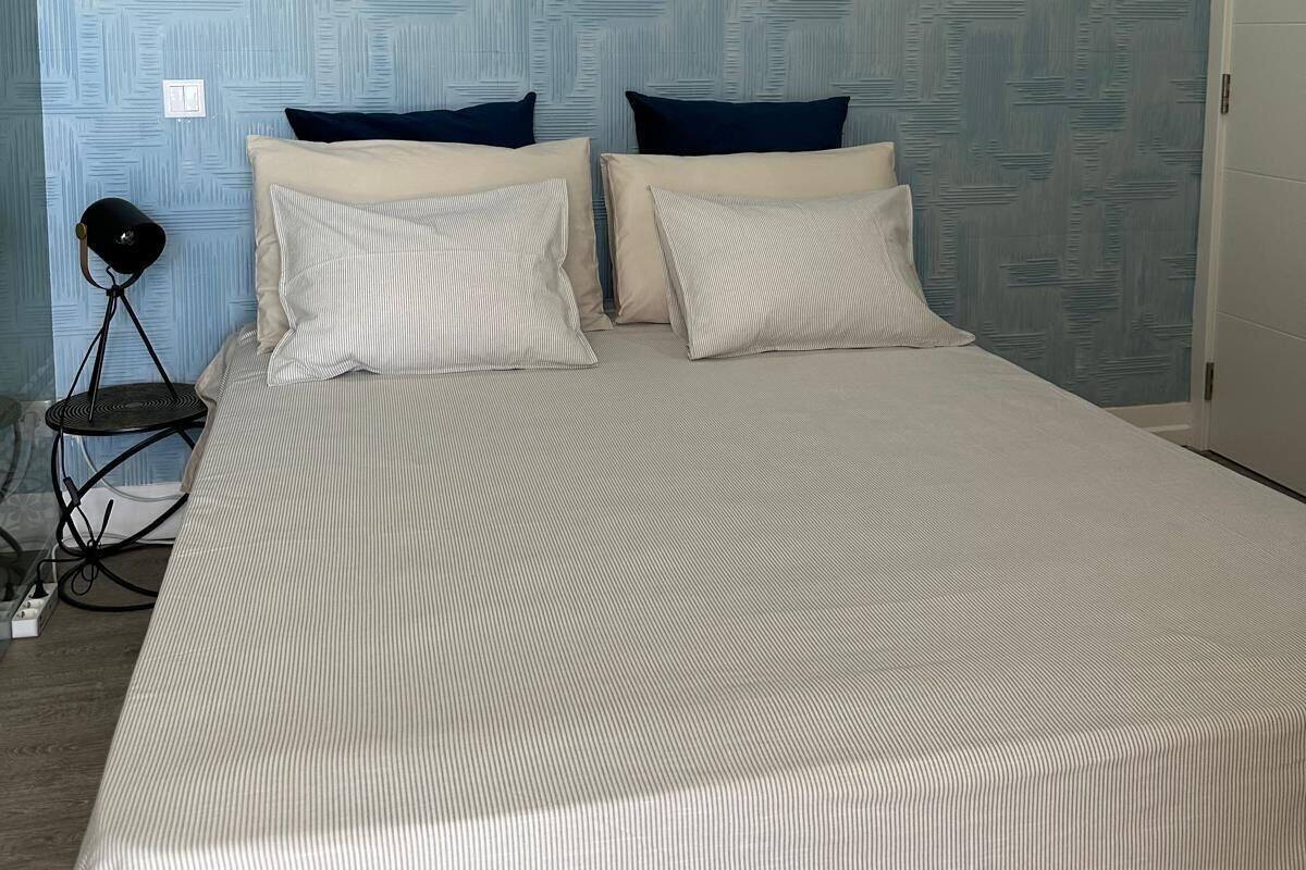 A bedroom with a bed, two pillows, a lamp, and a patterned wall.