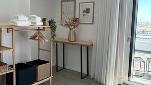 A modern, well-lit room with a wooden floor, a built-in wardrobe, a small table with a vase, and a view through a glass door. - Malpique Guest House & Jacuzzi (Albufeira)