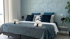 A modern bedroom with a large bed, a blue textured wall, and a wooden floor. - Malpique Guest House & Jacuzzi (Albufeira)
