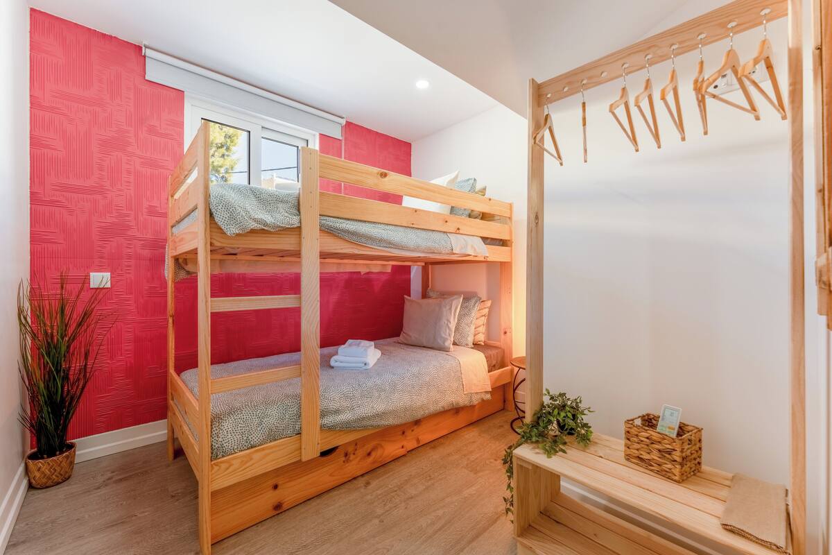 A bunk bed room with a red wall, wooden floor, and a small plant.