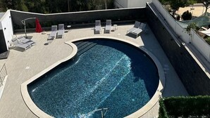 A rooftop swimming pool with lounge chairs and umbrellas, overlooking a coastal town with buildings and a clear sky. - Malpique Guest House & Jacuzzi (Albufeira)