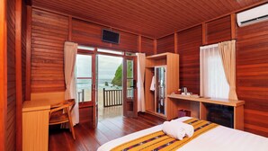 A wooden cabin room with a bed, a desk, a chair, and a view of the ocean. - Umarimba Beach Lodge (Mertak)