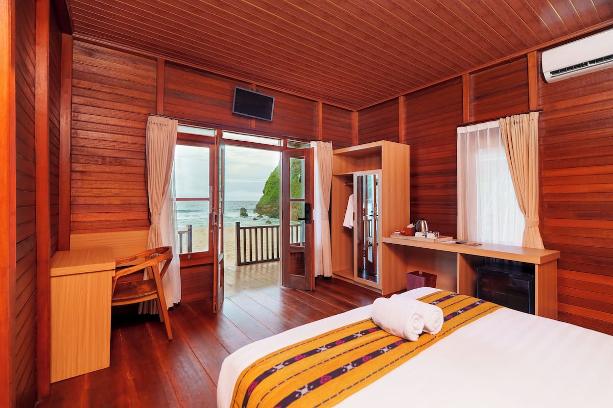 A wooden cabin room with a bed, a desk, a chair, and a view of the ocean.
