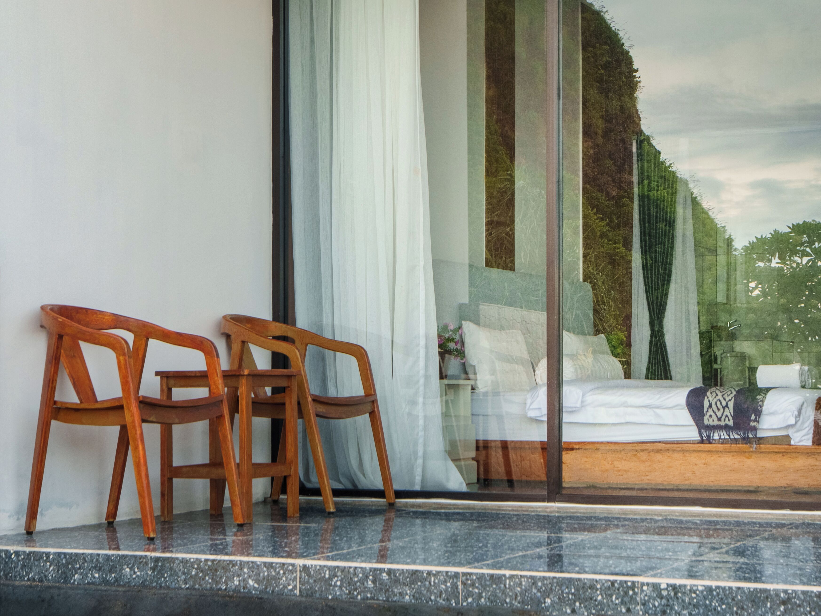 Una habitación con una cama, un ventanal con cortinas y dos sillas de madera.