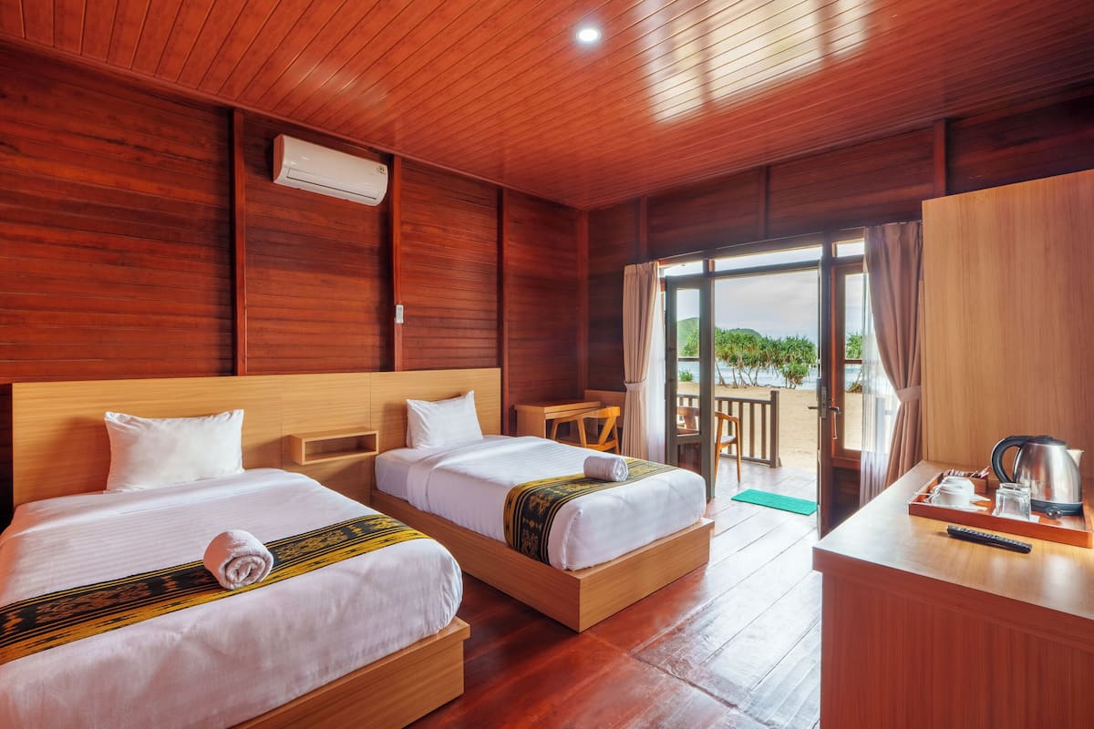 A hotel room with two beds, a desk, and a view of the outdoors.