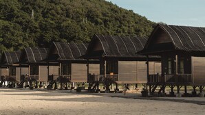 A row of wooden cabins with balconies, set on stilts, against a backdrop of a forested hill. - Umarimba Beach Lodge (Mertak)