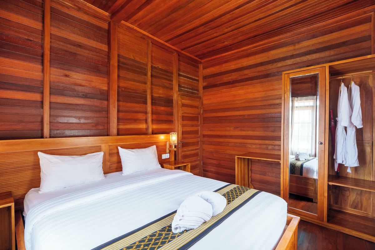A wooden-paneled room with a bed, a wooden wardrobe, and a mirror.