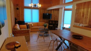 Uma sala de estar acolhedora, com piso de madeira, um sofá, uma mesa de jantar e uma TV fixada na parede.
