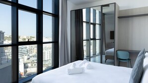 Ein modernes Hotelzimmer mit einem großen Bett, einem Schreibtisch und Blick auf die Stadt durch raumhohe Fenster.