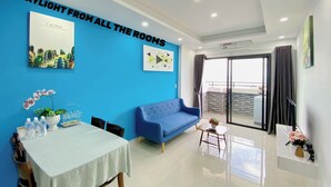 A modern living room with a blue wall, a sofa, a dining table with chairs, and a balcony with a view. - Ocean View Home Danang (Da Nang)