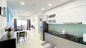 A modern kitchen with white cabinets, a stainless steel refrigerator, a black countertop, and a dining area with a table and chairs. - Ocean View Home Danang (Da Nang)