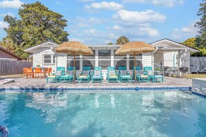A swimming pool with lounge chairs and umbrellas, a wooden deck, and a house in the background. - Seaside Paradise: Dive into Luxury with Saltwater Pool, Spa, and Chemical-Free Bliss (Ponte Vedra Beach)