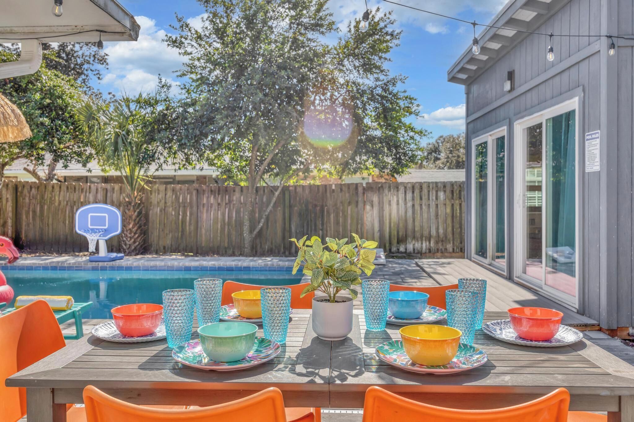 An outdoor dining area with a pool, a basketball hoop, and a wooden fence in the background.