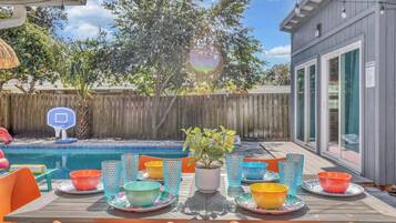 An outdoor dining area with a pool, a basketball hoop, and a wooden fence in the background.